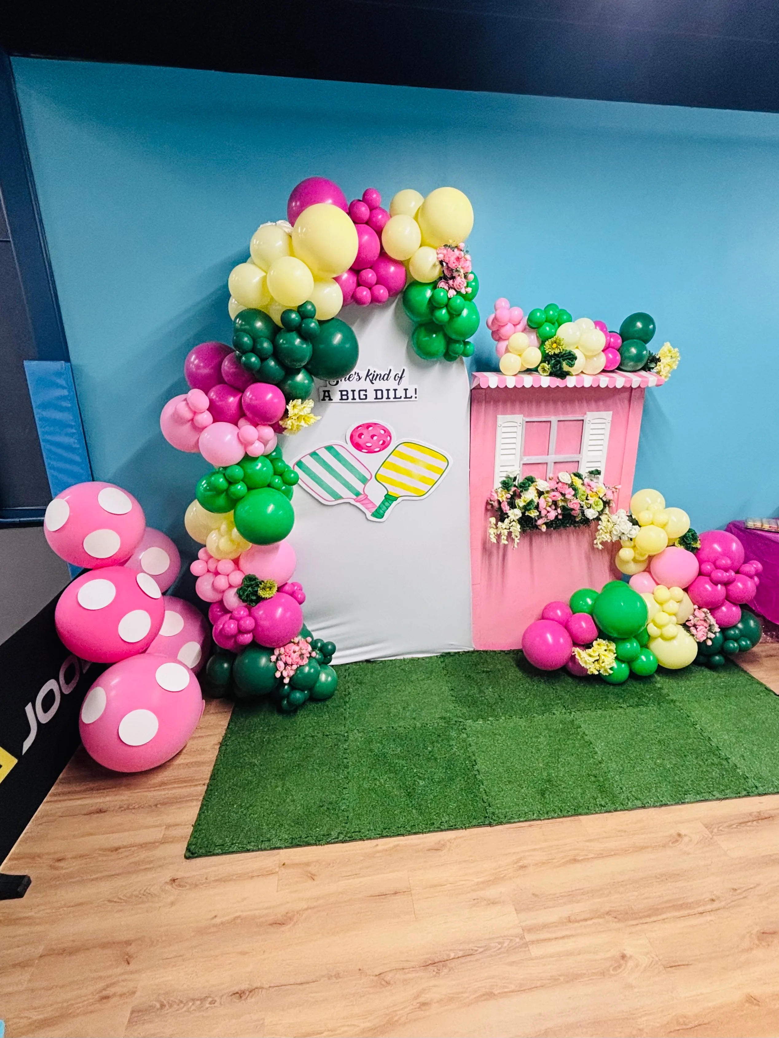 Summer-themed party setup with colorful balloon garlands, popsicle decor, and a floral pink window prop.